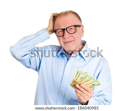 Closeup portrait, nerd senior mature man, black glasses, holding money in one hand, scratching head, not sure how to spend extra cash dollar bills, isolated white background. Human emotion, expression