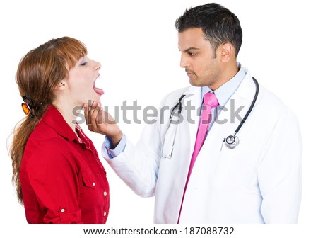 Closeup portrait, health care professional performing oral, throat, neck physical exam holding face looking inside mouth of patient woman standing saying ahhhh, isolated, white background.