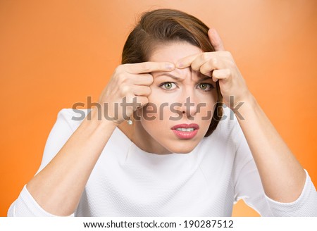 Closeup portrait, young pretty beautiful frustrated woman surprised stunned to see zit on her face, isolated orange background. Negative emotion facial expression feelings, situation, reaction