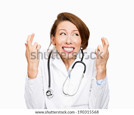 Closeup portrait, young health care professional, stressed female doctor, crossing fingers, praying, hoping best patient outcome, isolated white background. Human face expressions, emotions, reaction