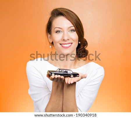 Closeup portrait, young woman, dealership, customer service agent holding model black car, offering credit line, lease deal, new inventory isolated orange background. Automobile purchase, financing.