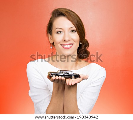 Closeup portrait, young woman, dealership, customer service agent holding model black car, offering credit line, lease deal, new inventory isolated red background. Automobile purchase, financing.