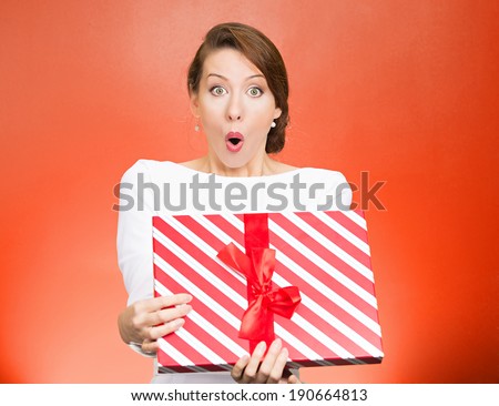 Closeup portrait happy super excited, surprised young woman, received unexpected gift box,opened eyes, mouth isolated orange background. Positive emotion, facial expression feeling, attitude, reaction