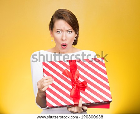 Closeup portrait young woman holding opening gift box, displeased, shocked angry disgusted with what received, isolated yellow background. Negative human emotion, facial expression, feeling, reaction