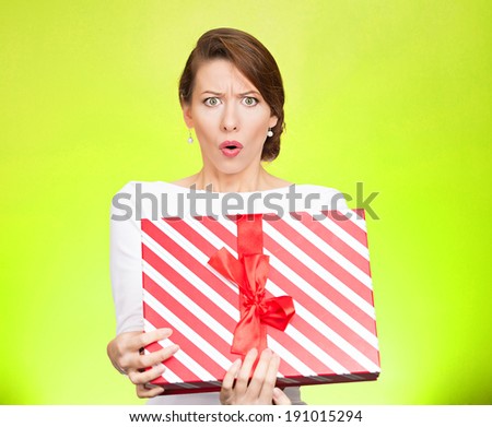 Closeup portrait young woman holding opening gift box, displeased, shocked angry, disgusted with what received, isolated green background. Negative human emotion, facial expression, feeling, reaction