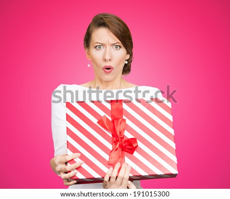 Closeup portrait young woman holding opening gift box, displeased, shocked angry, disgusted with what received, isolated pink background. Negative human emotion, facial expression, feeling, reaction