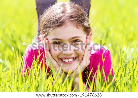 Closeup portrait sweet little, happy, cute, smiling, relaxed excited girl, light brown hair, laying, sitting green grass isolated outdoors background. Childhood, positive emotion, facial expressions