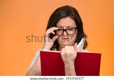 Closeup portrait, mature woman with black eye glasses trying to read book, having difficulties seeing text because vision problems. Negative emotion facial expression feelings reaction, health issues