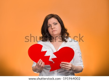 Closeup portrait middle aged, troubled, sad, confused woman, holding broken heart in hands, thinking, isolated orange background. Negative human emotion, facial expression, feelings, life reaction