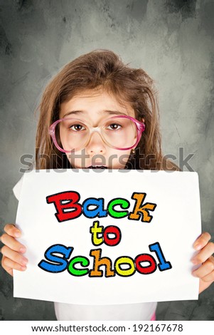 Closeup portrait sad, unhappy, stressed tired, overwhelmed, funny looking little girl with messed up glasses, holding back to school sign, isolated dark background. Facial expression, emotion, feeling