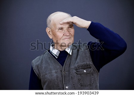 Closeup portrait happy senior, elderly, old man, grandfather looking afar, horizon, future, covering face from sun, isolated, black, blue background. Human face expressions, emotions, life perception