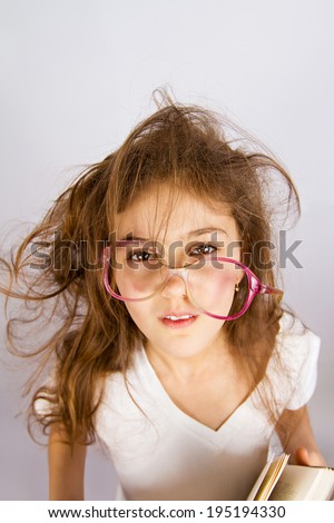 Closeup portrait confused unhappy stressed tired, funny looking little girl with messed up hair, glasses holding book having multiple unanswered questions isolated grey background. Facial expression