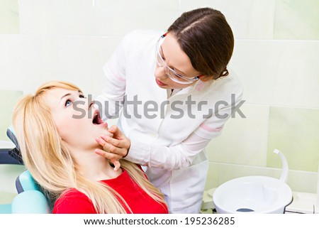 Closeup portrait young female dentist, doctor, health care professional working, carrying out thorough examination, patient seating in chair, wide open mouth, isolated background stomatology office