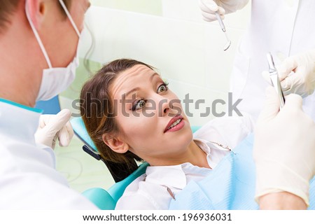 Closeup portrait young terrified girl woman scared at dentist visit, siting in chair, funny looking with fear, doesn\'t want dental procedure drilling tooth extraction isolated clinic office background