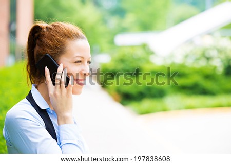 Closeup portrait smiling happy businesswoman talking on mobile phone. Business woman having conversation on cellphone standing in front corporate office. Company employee isolated background trees
