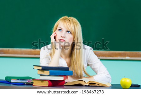 Closeup portrait annoyed bored tired woman, student sitting at desk, looking up, fed up studying, daydreaming thinking isolated green chalkboard background. Face expression, emotion, reaction attitude