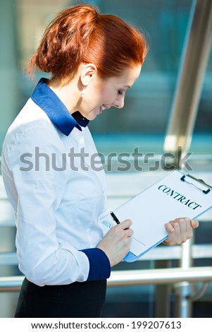 Closeup portrait smiling young business woman, company employee holding contract document pointing with pen at space for signature isolated corporate office background Positive face expression emotion