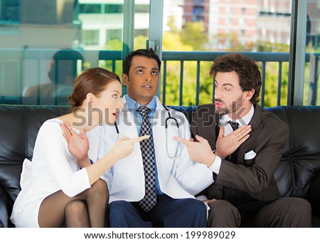 Closeup portrait psychiatrist sitting on black couch caught in between angry couple man, woman trying to push them back in doctor\'s office isolated city urban background. Negative emotion. Healthcare
