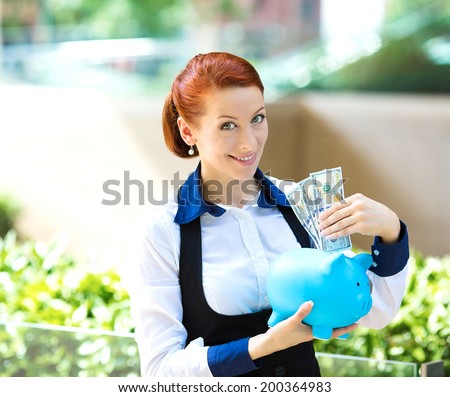 Closeup portrait happy business woman, bank employee holding piggy bank, dollar bills isolated outdoors corporate office background. Financial savings concept. Positive human emotion facial expression