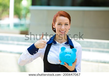 Closeup portrait happy, smiling business woman, bank employee holding piggy bank, isolated outdoors corporate office background. Financial savings, banking concept. Positive emotion face expression