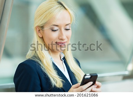 Closeup portrait, happy, blonde girl, smiling,  looking at company cell phone, isolated background corporate office. Facial expression, reaction. Business woman sending text message from her mobile.