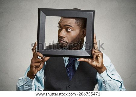Closeup portrait businessman executive looking sideways, curious surprised confused through black picture frame thinking beyond borders accepted rules isolated grey background. Face expression emotion