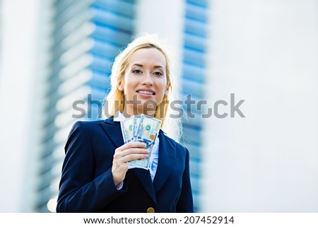 Closeup portrait super happy excited successful young business woman holding money dollar bills in hand isolated corporate office background. Positive emotion face expression feeling. Financial reward