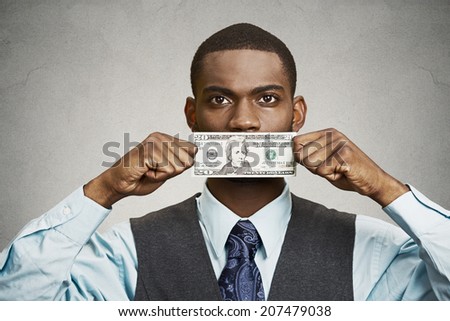 Closeup portrait handsome young corrupt corporate man in blue shirt holding twenty dollar bill to mouth, isolated grey background. Bribery concept in politics, business, diplomacy. Life perception