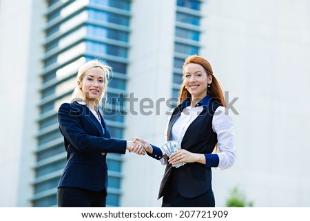 Closeup portrait happy excited successful two young business women, banker, customer one giving to other money isolated corporate office background. Positive emotion face expression. Financial reward