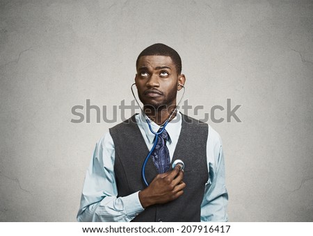 Closeup portrait executive man, business person, worker listening to his heart with stethoscope looking up isolated grey background. Preventive medicine, financial condition concept. Face expressions