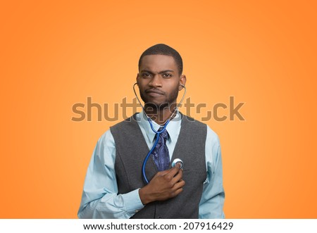 Closeup portrait serious executive man, business person, worker listening to his heart with stethoscope isolated orange background. Preventive medicine, financial condition concept. Face expressions