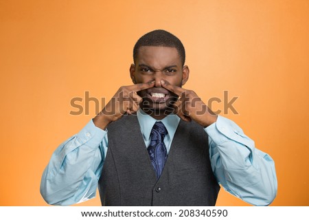 Closeup portrait young executive man, disgust on face, pinches his nose, something stinks, bad smell, situation isolated orange background. Negative emotion facial expression perception body language
