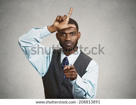 Closeup portrait angry mad young Unhappy Man, student displaying Loser Sign on forehead, pointing at you with disgust, isolated grey background. Negative human emotion, facial expression Body Language