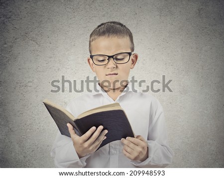 Closeup Portrait Unhappy Child, Boy holding Reading Book, displeased with story, information provided, isolated grey Wall Background. Negative human facial expression, emotions, feeling, body language