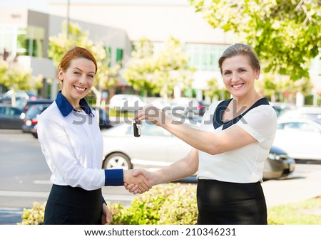 Portrait two happy, excited business women one giving to customer car or home keys, isolated outdoors dealership lot background. Positive face expressions, life perception, Banking, finance concept.