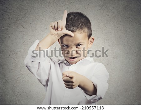 Closeup portrait angry young Unhappy boy, young student displaying Loser Sign on forehead, pointing at you with disgust isolated grey wall background. Negative human emotion, expression Body Language
