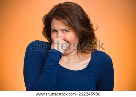 Closeup portrait middle aged woman who covers, pinches her nose with hand looks with disgust, something stinks, bad smell, situation, isolated orange background. Human face expressions, body language
