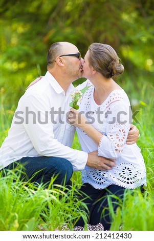 Portrait happy, kissing mature couple, husband, wife hugging each other, relaxing on summer sunny day in park, outside on green grass. Positive human expressions, emotions, feelings, life perception