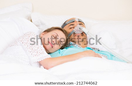 Man with sleeping apnea and CPAP machine, devise, asleep peacefully with wife in bedroom their house. Healthcare management patient with sleep apnea. Human respiratory, airway, system health issues.