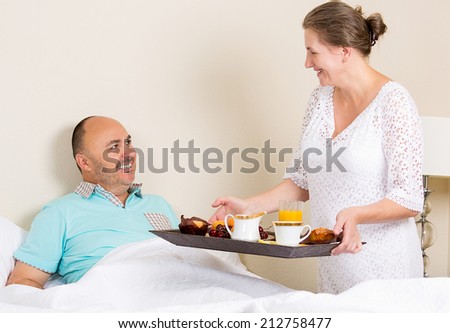 Wife bringing breakfast in bed to delighted husband in bedroom at home. Positive emotions, face expressions, feelings. Happy family life, strong relationship concept.