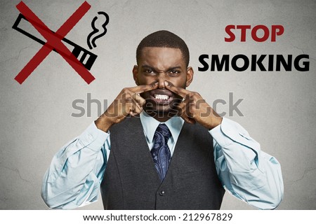 Portrait young man, pinches his nose, something stinks bad smoke smell, grey wall background, stop smoking sign. Negative face expression, body language, reaction Smoking restricted area. Breath smell