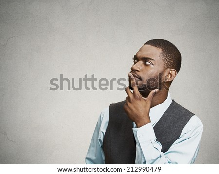 Side view portrait young, puzzled business man thinking, deciding about something, finger on lips, looking up, confused isolated grey wall background with copy space. Emotion facial expression feeling