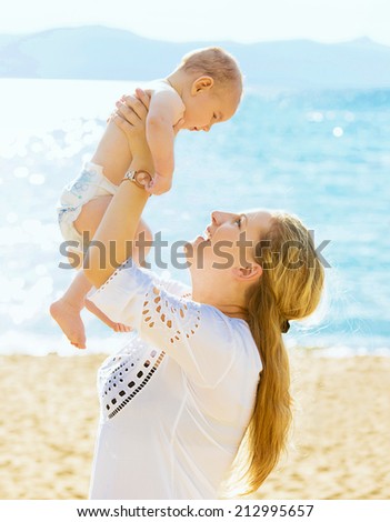 Happy family. Young mother throws up baby in the sky isolated outside sea, mountains background on sunny day. Portrait mother and little son on the beach. Positive human emotions, feelings, emotions.