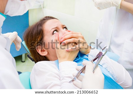 Closeup portrait young terrified girl woman scared at dentist visit, siting in chair, covering her mouth, doesn\'t want dental procedure, drilling, tooth extraction, isolated clinic office background