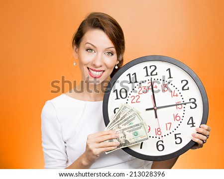 Closeup portrait happy young business woman, corporate employee, ceo holding wall clock, dollar bills in hands. Time is money concept isolated orange background. Positive human emotion face expression