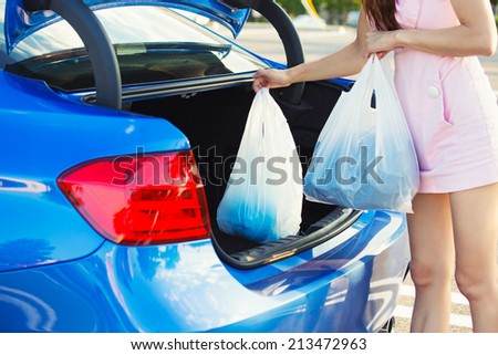 Cropped image of woman putting shopping bags inside trunk of her blue car, on a mall, store, supermarket parking lot