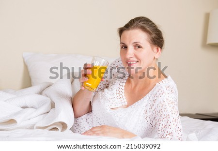 Happy middle aged, beautiful woman having breakfast, relaxing in hotel bed, bedroom of her house drinking orange juice, vacation, weekend time. Positive human emotions, face expressions, feelings