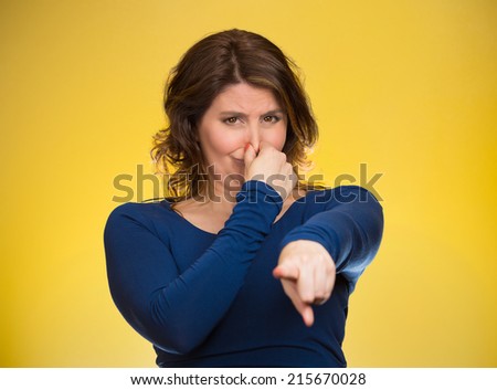 Portrait unhappy woman pinches nose, looks displeased, pointing at you with finger something, you stink, bad smell isolated yellow background. Human facial expressions, emotions, feelings, reaction