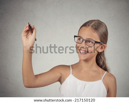 Closeup portrait happy teenager girl student with glasses writing with pen on blackboard, isolated grey wall background with copy space. Education, knowledge concept. Positive face expression emotion