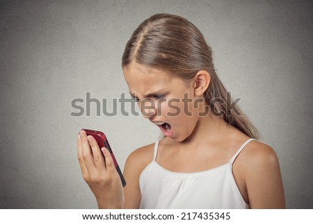 Closeup portrait young mad, frustrated angry teenager girl yelling while on phone isolated grey wall background. Negative human emotion facial expression feelings. Communication, conflict resolution